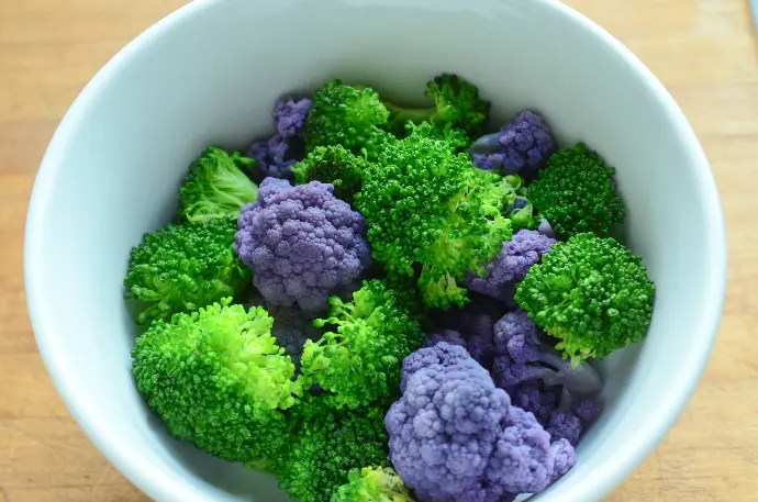 A white bowl filled with purple and green broccoli